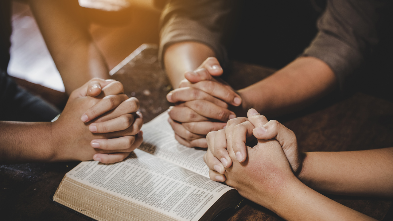 3 set of hands clasped together resting on a bible